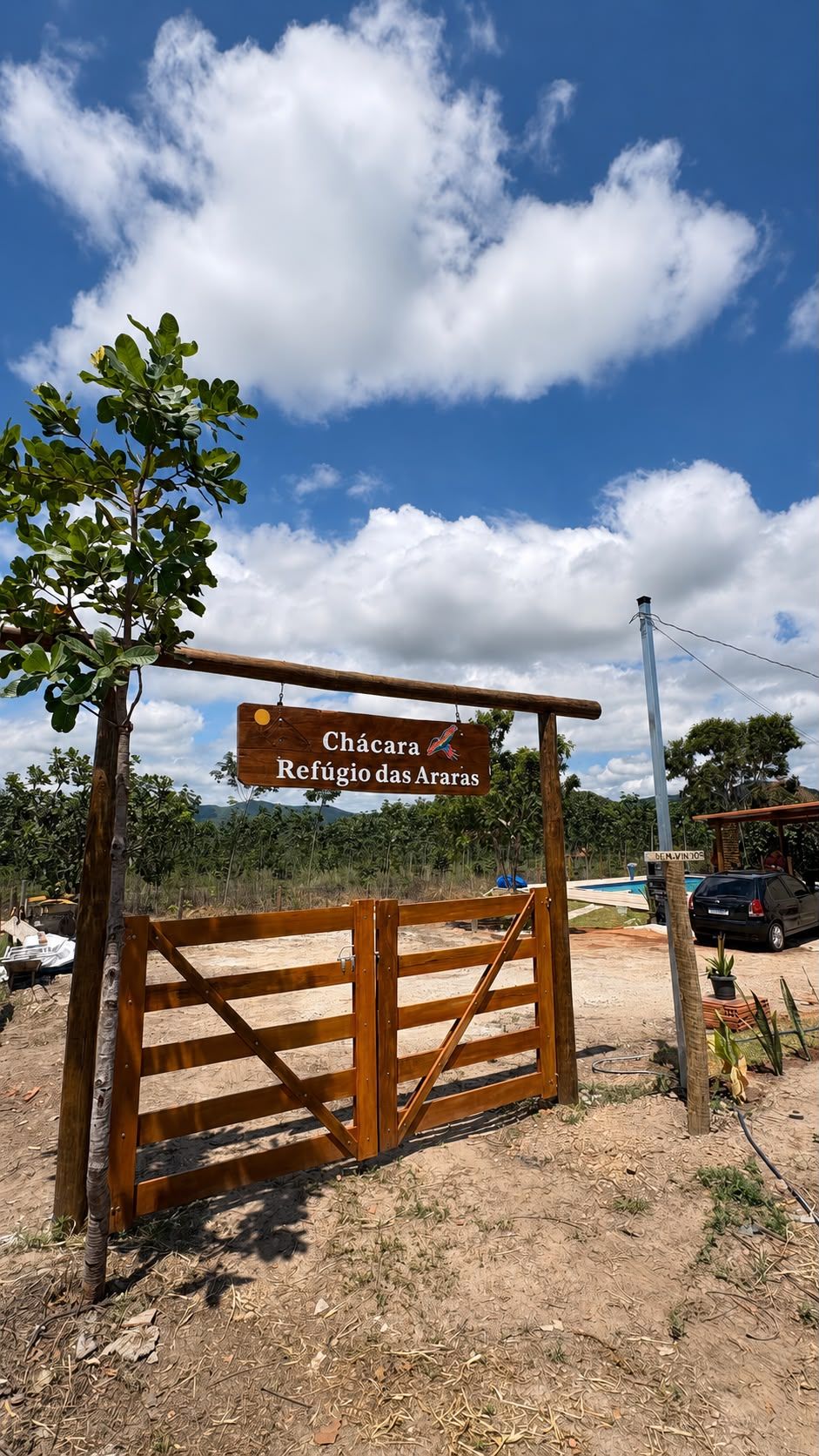 Portão de entrada da chácara com a placa 'Chácara Refúgio das Araras' pendurada, cercado pelo Cerrado de Pirenópolis